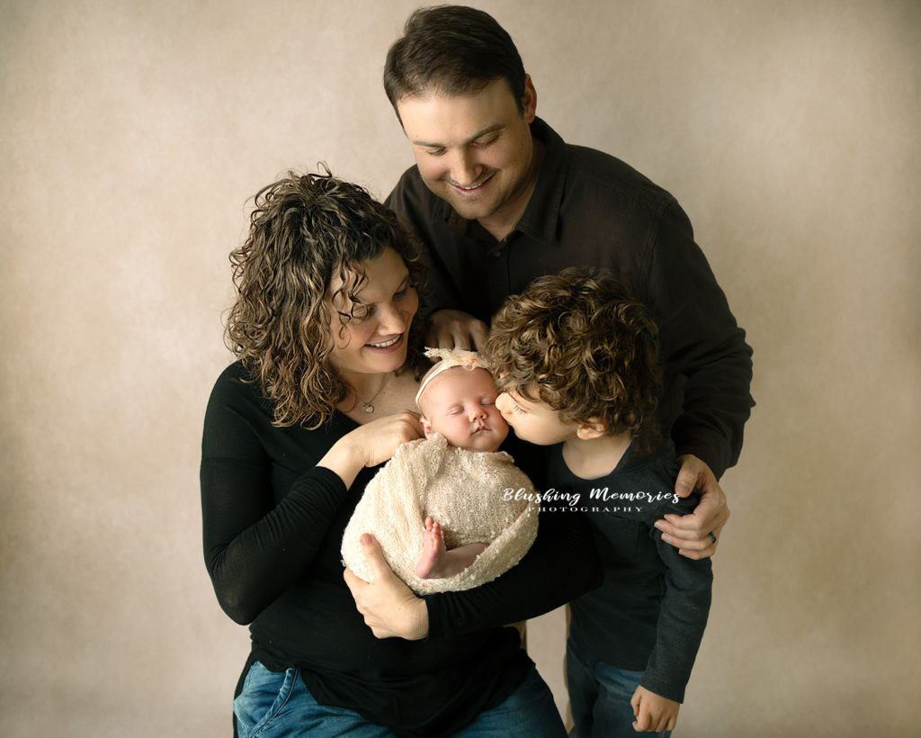 Big brother kissing her newborn baby girl sister for a family photo portrait session