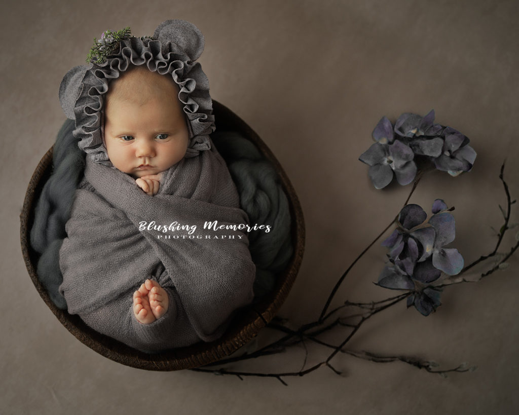 newborn baby girl with hydrangea flower around her and bonnet