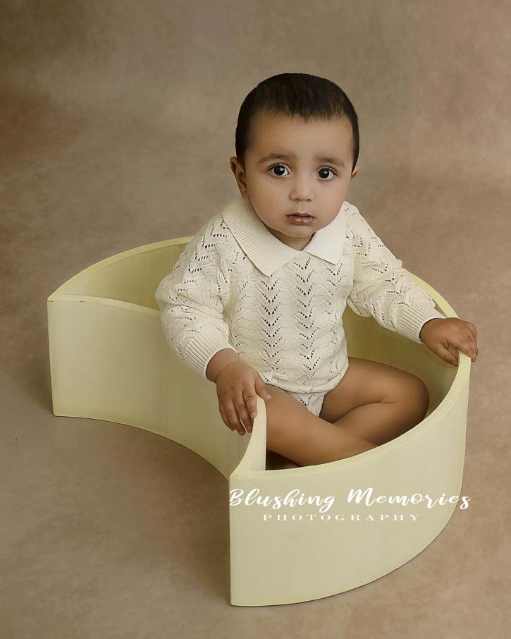 portrait photoshoot of a boy in a moon shaped prop for his first birthday