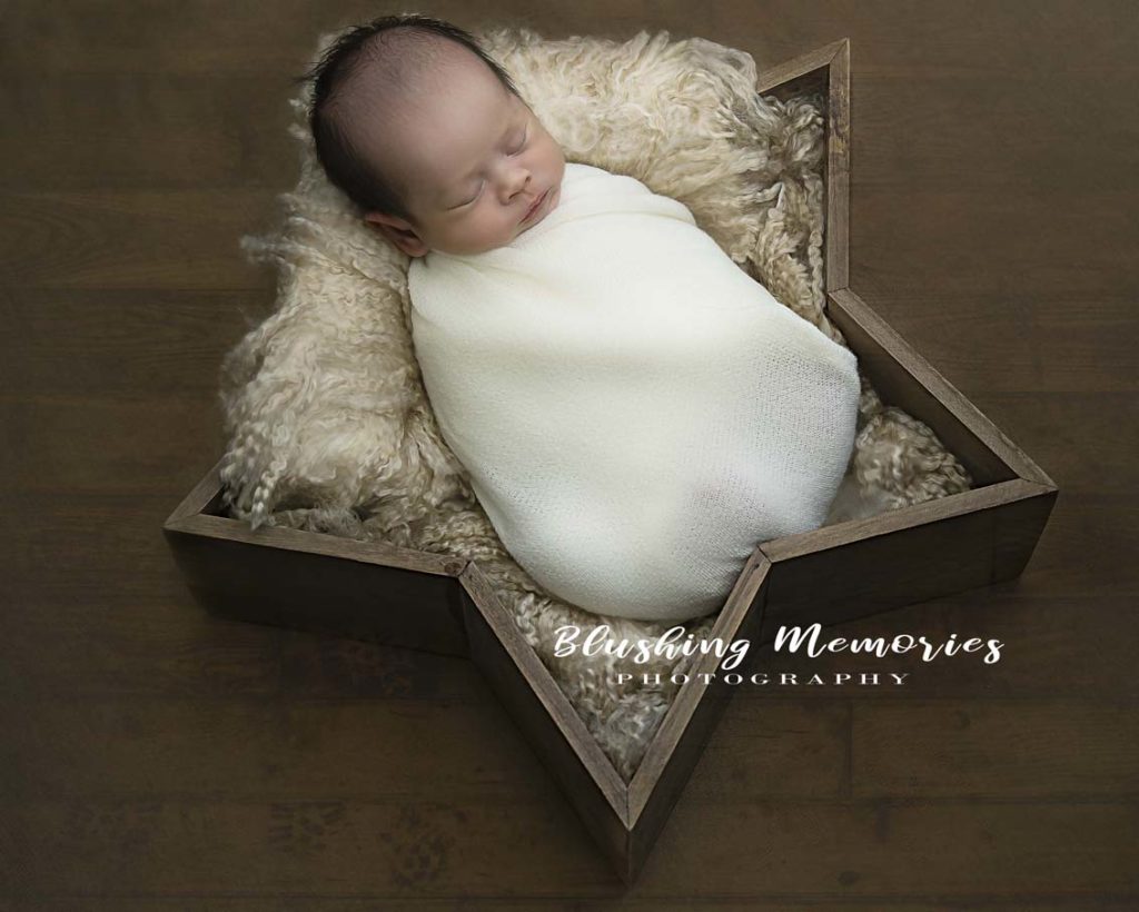 newborn baby boy posed in a star shaped prop for a studio photoshoot