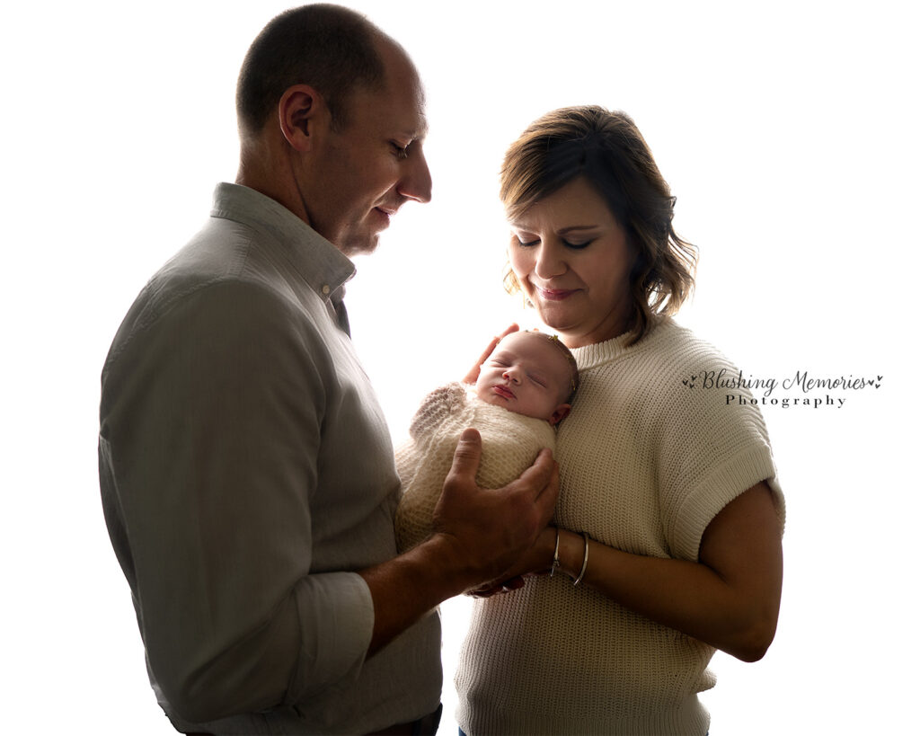 newborn baby girl photo wither her mom and dad holding her at studio of Blushing Memories, El Dorado Hills