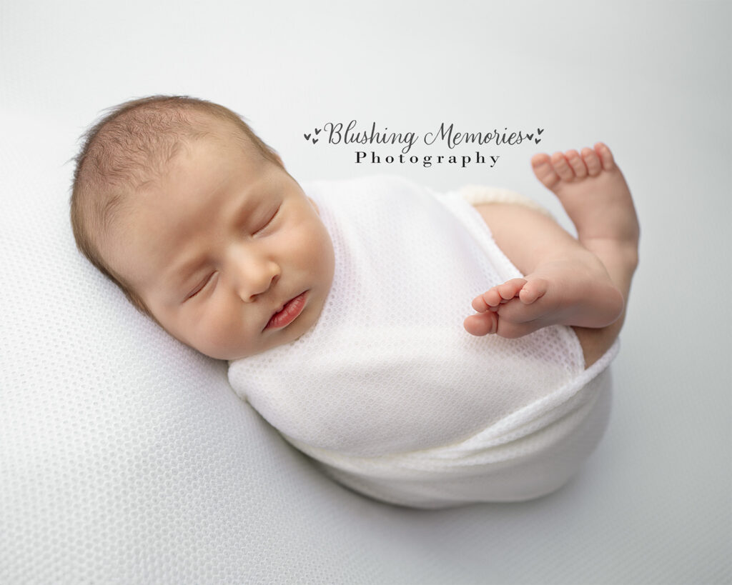 Newborn baby boy peacefully sleeping wrapped in soft white blanket – Blushing Memories Photography studio session