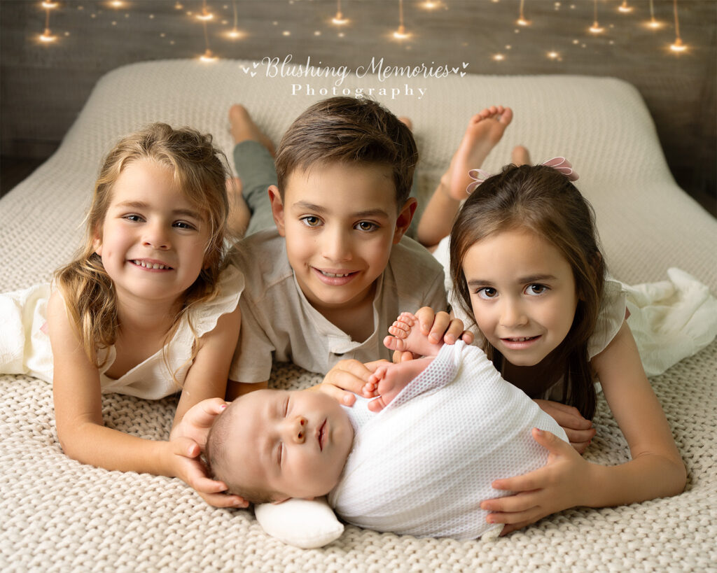 Newborn Baby boy with siblings on the bed, at Blushing memories Studio in El Dorado hills