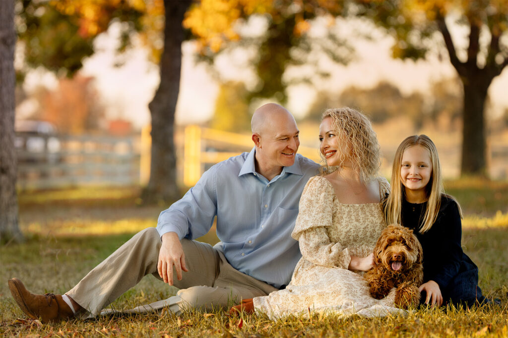 A loving family enjoying a fall outdoor photo session with their daughter and dog, captured by Blushing Memories Photography in Folsom, California.