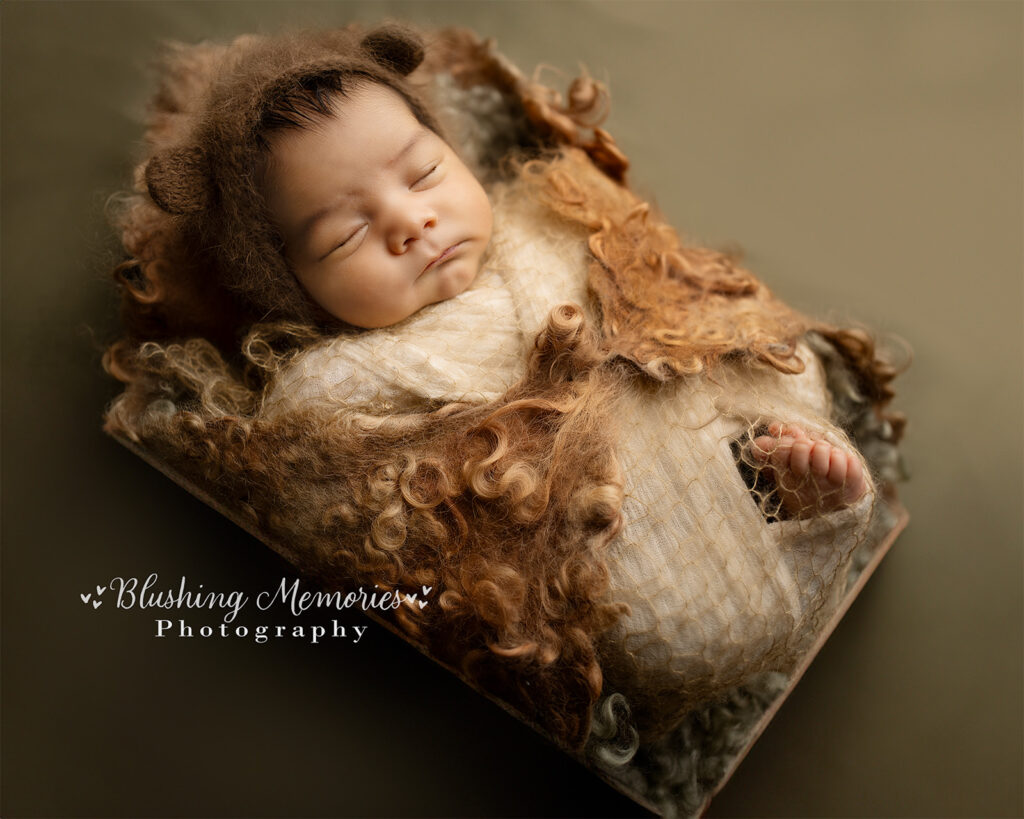 A newborn baby boy peacefully sleeping, wrapped in a brown beige felted wrap, photographed at Blushing Memories Photography Studio in El Dorado Hills, California.