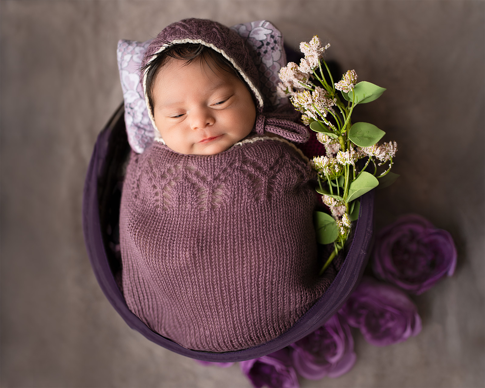 Newborn baby girl wrapped in purple fabric with floral styling during a newborn photography session in Folsom CA