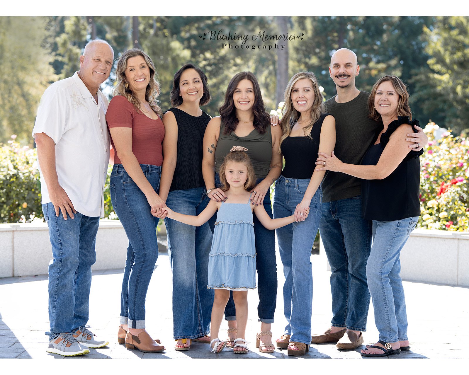 A multi-generational family from Roseville posing together outdoors in casual attire, with a young girl in a blue dress standing in the center for a portrait.